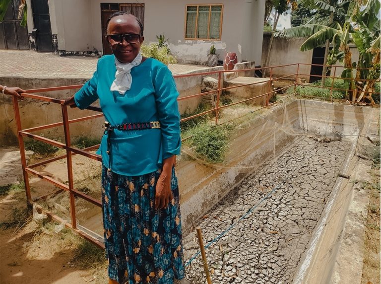 Anna Lulandala with a hopeful smile, standing beside her fishpond at home.